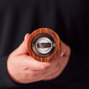 #salt A person holds a Portobello Olive Wood Salt & Pepper Mill by Cole & Mason upside down, focusing on the adjustable grind metal mechanism. The individual's hand and part of a dark sleeve are visible.