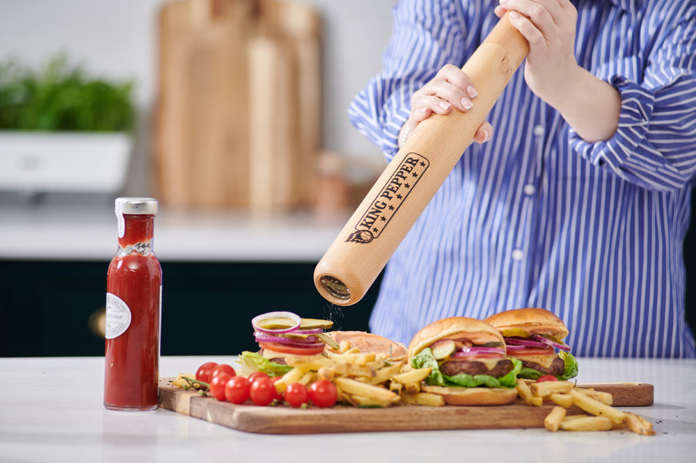 A 710mm King Pepper Baseball Bat Pepper Mill by Cole & Mason UK stands upright on an off-white background, its light natural finish features a Tiny Peppy logo near the bottom and a design inspired by the classic King Pepper mill.