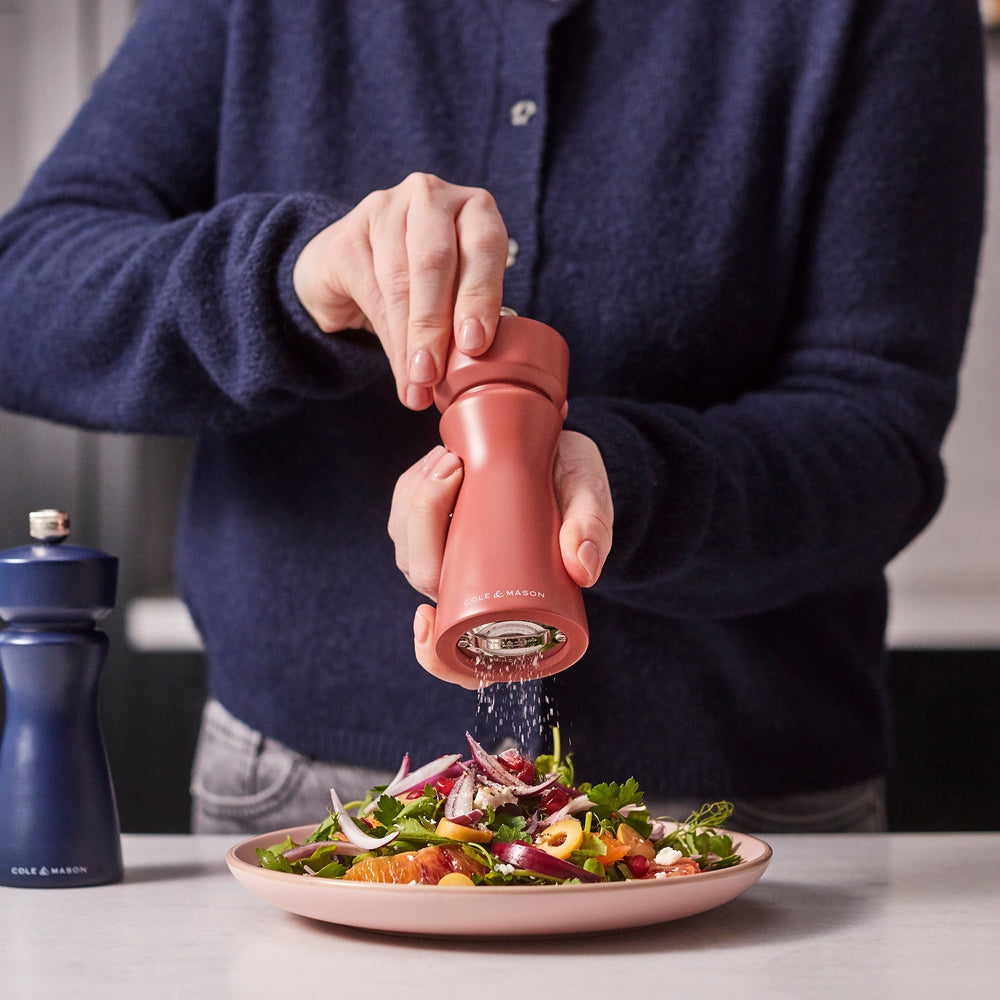 A matte, cinnamon-colored salt and pepper mill with a rounded top and curved body, featuring COLE & MASON in white text at the base, set against a plain, light background. The Kenton Salt & Pepper Mill by Cole & Mason is a stylish kitchen accessory equipped with a durable ceramic grinder for efficient seasoning.