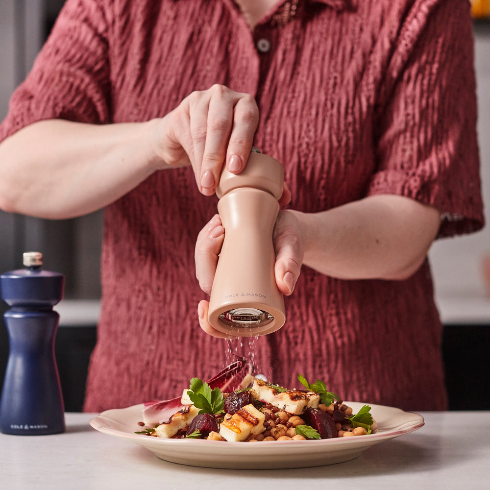 A Cole & Mason Kenton Salt & Pepper Mill in Himalayan Salt, featuring a modern, curved design with a metal knob on top and a durable ceramic grinding mechanism, is set against a plain, light background.
