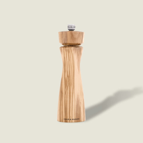 #salt The Cole & Mason Portobello Olive Wood Salt & Pepper Mill, featuring a natural wood grain finish, silver top knob, and precision grinding mechanism, stands upright against a light beige background.