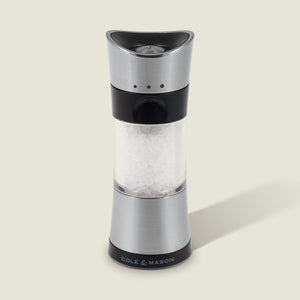 A Cole & Mason Horsham Salt & Pepper Mill in stainless steel and clear acrylic, filled with coarse salt, stands upright on a light background with a right-side shadow and the COLE & MASON logo at its base.