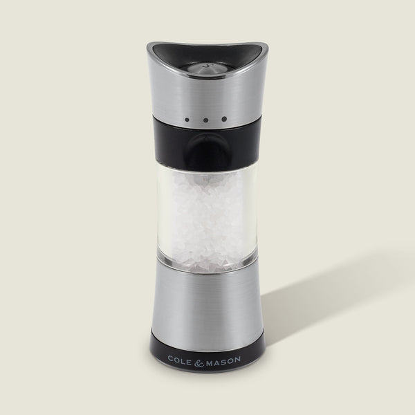 A Cole & Mason Horsham Salt & Pepper Mill in stainless steel and clear acrylic, filled with coarse salt, stands upright on a light background with a right-side shadow and the COLE & MASON logo at its base.